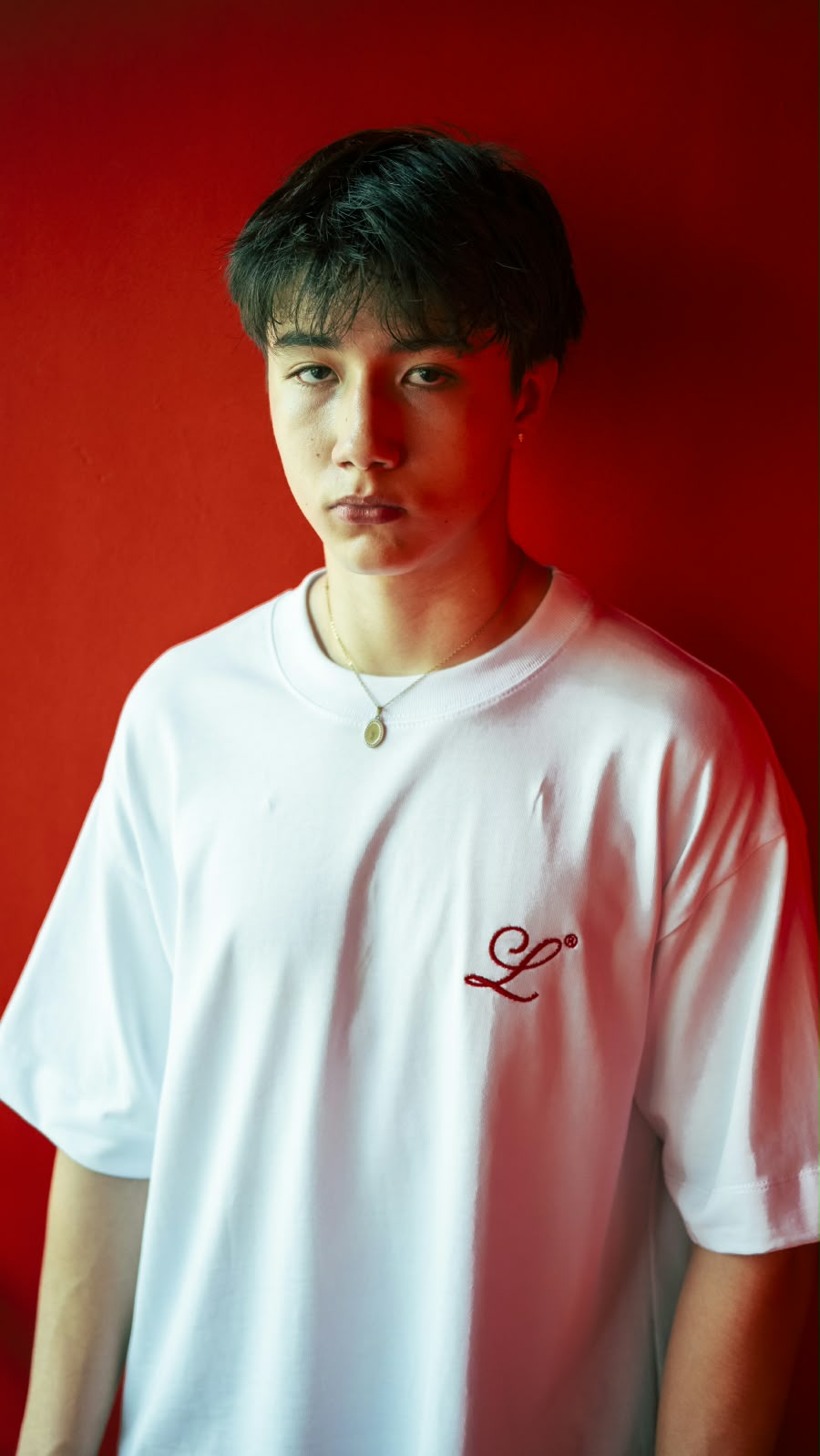Modelo usando camiseta blanca boxy fit Legendary Immortal God con monograma L bordado en rojo en el pecho.