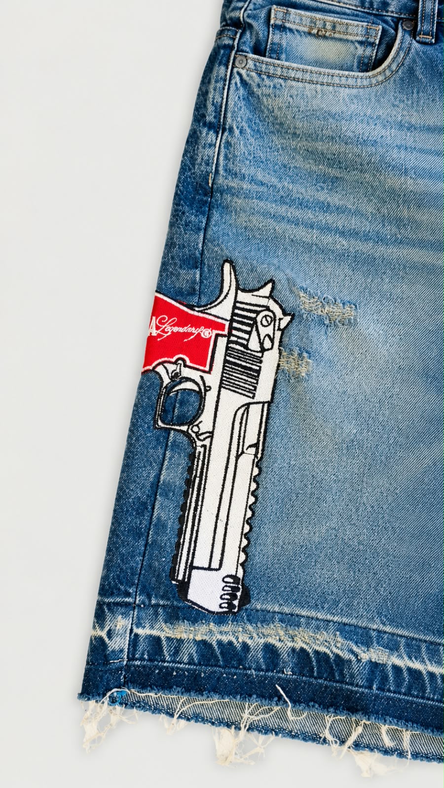 Bordado gráfico de pistola Legendary en short denim azul con acabado desgastado.