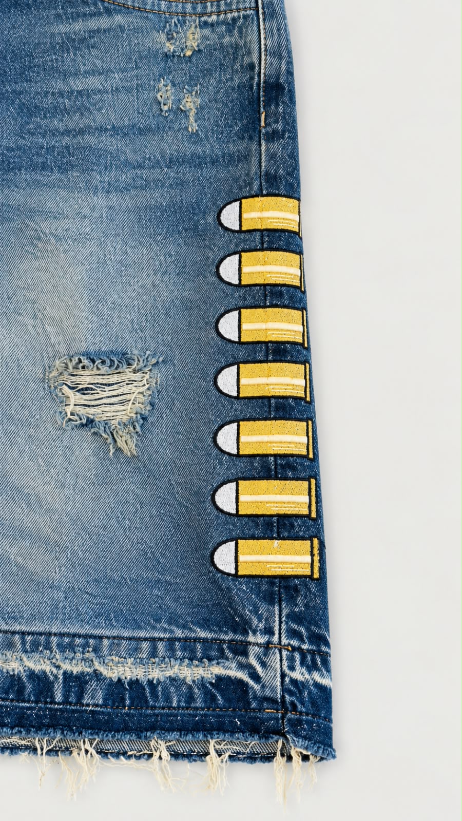Detalle de short denim azul Legendary Mafia con bordados de proyectiles amarillos y acabado desgastado.
