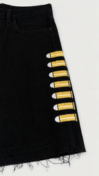 Detalle de short denim negro Legendary con bordados de proyectiles amarillos y bajo deshilachado.