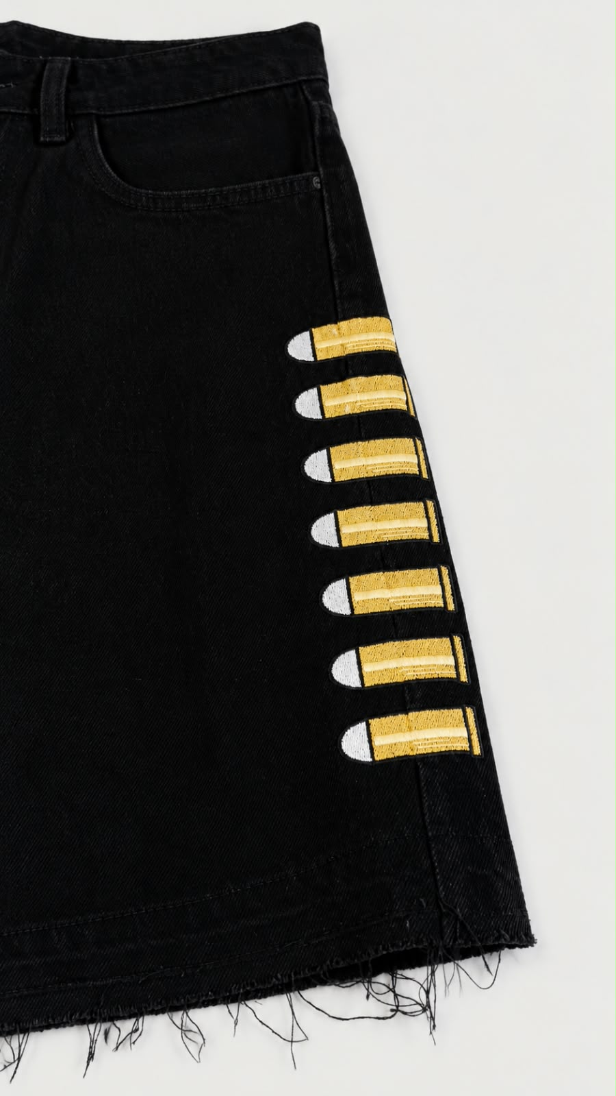 Detalle de short denim negro Legendary con bordados de proyectiles amarillos y bajo deshilachado.